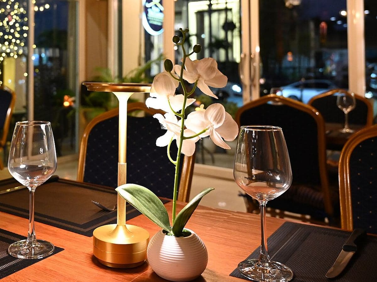 A restaurant table set for two, with a glowing lamp and an orchid
