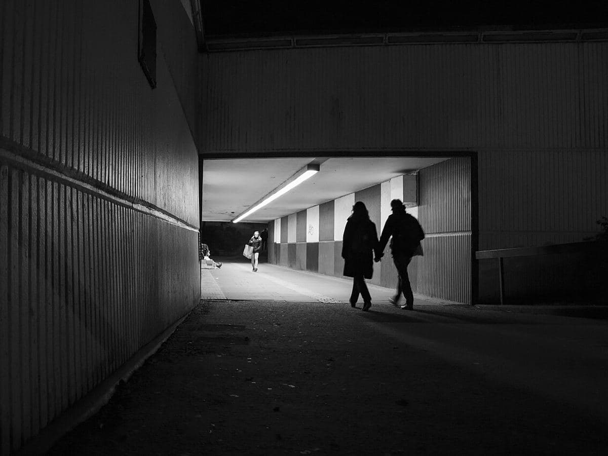 Two people holding hands as they walk through an underpass at night
